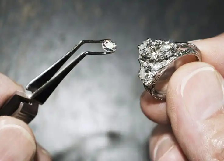 Close-up of a jeweler replacing a loose diamond in a silver engagement ring using precision tweezers in Milton.